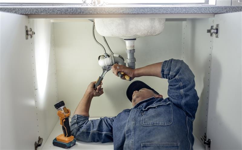 Plumber repairing pipes beneath a bathroom sink in Lafayette