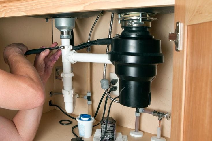 Plumber installing a garbage disposal beneath a kitchen sink in Lafayette