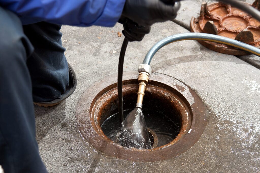 Plumber hydro jetting a sewer line through a manhole in Lafayette