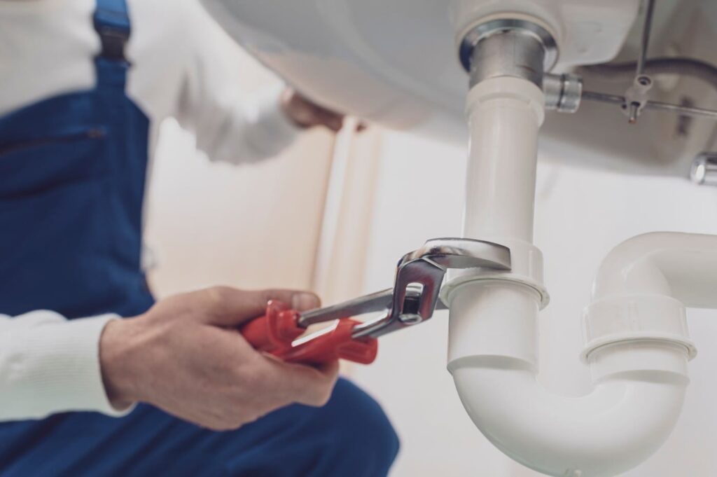 Plumber repairing a white drain pipe beneath a sink in Lafayette