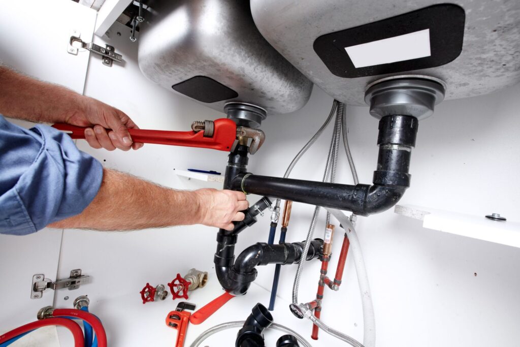 Plumber repairing drain pipes beneath a kitchen sink in Lafayette