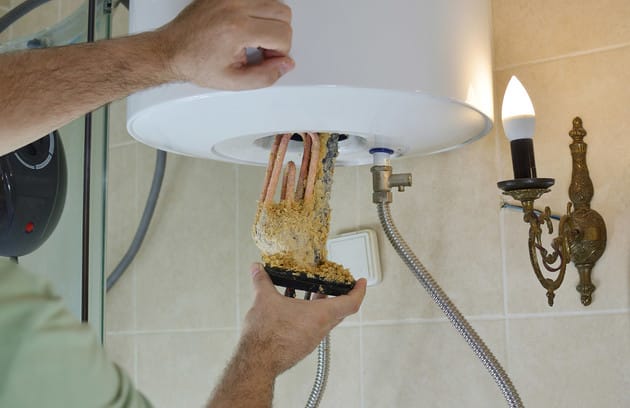 Technician removing mineral buildup from a water heater in Lafayette